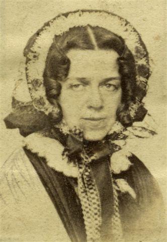 A sepia toned photograph of Elizabeth Carne, the Cornish author, philanthropist, and natural historian. It shows a middle aged woman in a bonnet. She has dark, centre parted ringlets and is looking directly into the camera.